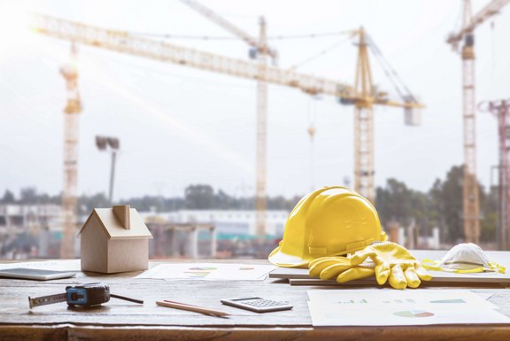 Tisch mit einem Gebäudemodell aus Holz, einem Bauhelm, Pläne und weitere Utensilien